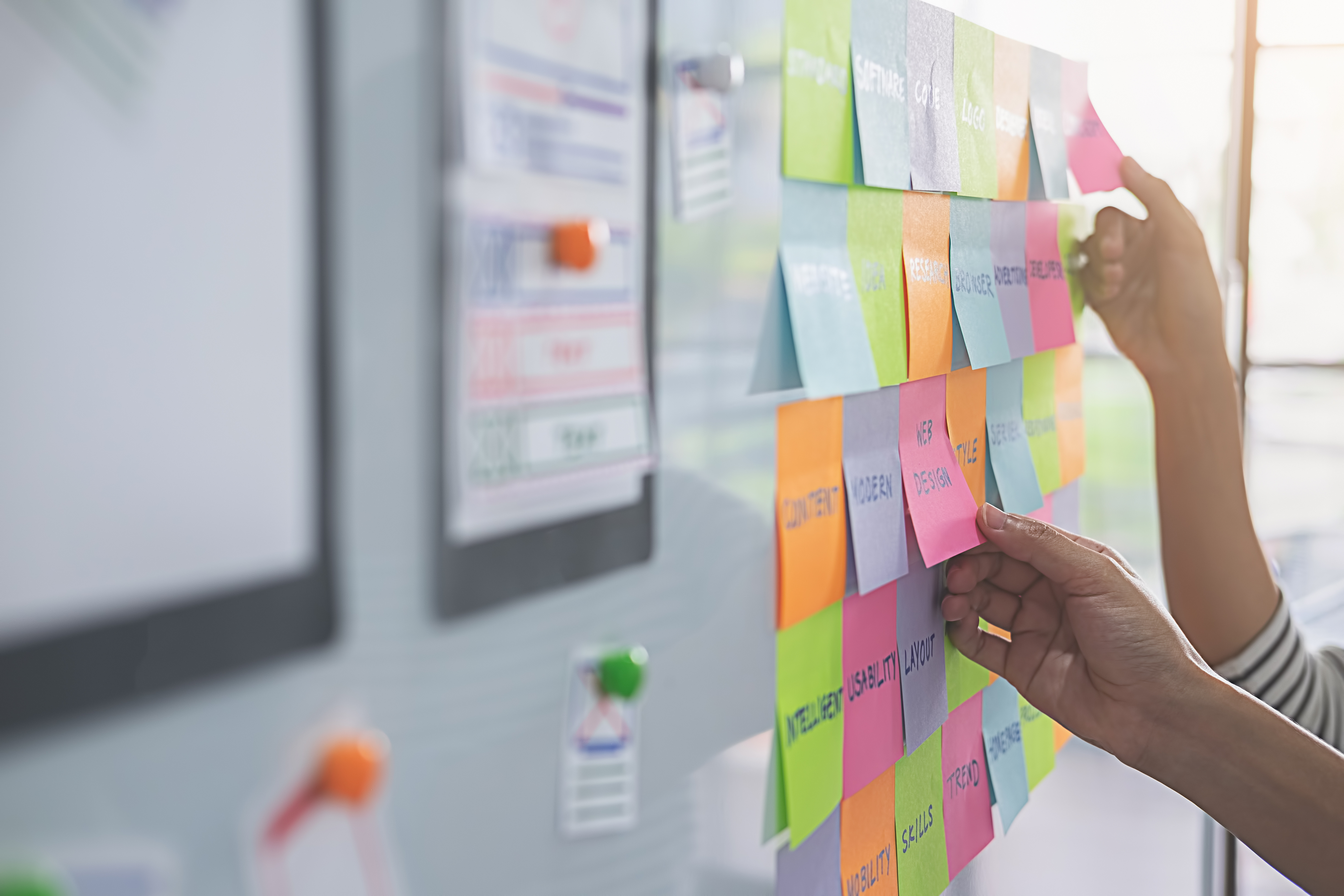 two peoples' hands arranging sticky notes on a board