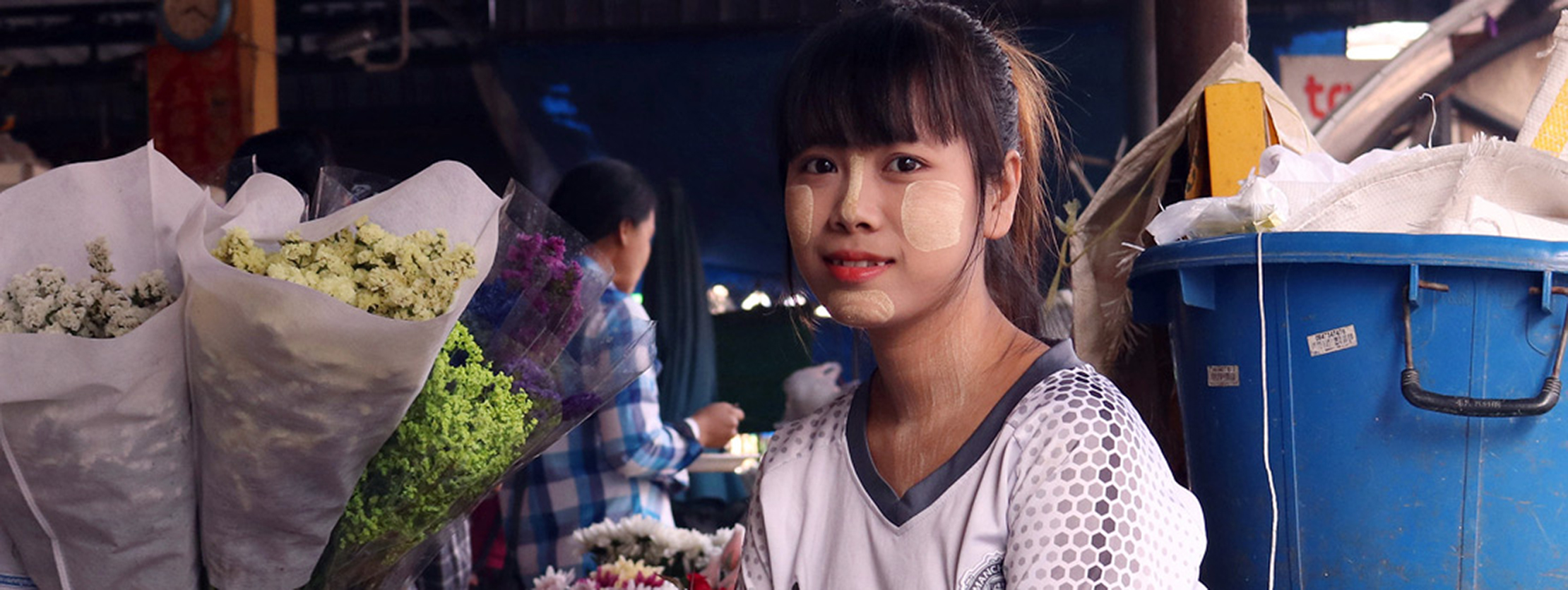 Young woman in a flower market with traditional face paint, surrounded by colorful bouquets of fresh flowers
